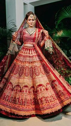 a woman in a red and gold bridal gown is posing for the camera with her hand on her hip