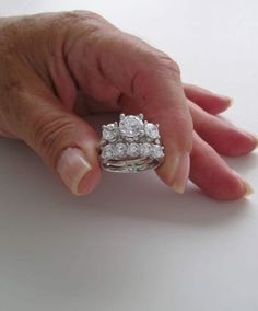 a woman's hand holding a diamond ring on top of her finger, with the other hand