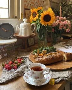 a wooden table topped with a cup of tea next to a loaf of bread and strawberries