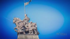 a statue with a flag on top of it in front of a bright blue sky