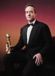 a man in a tuxedo is holding a golden trophy and posing for the camera