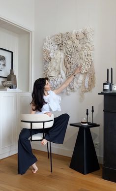 a woman sitting on a chair in front of a wall hanging