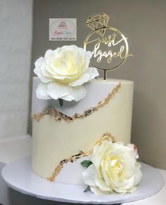 a wedding cake with white flowers on top and gold decoration around the edges, sitting on a table