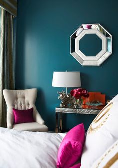 a white chair sitting next to a bed under a mirror mounted on the side of a wall