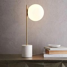 a white table lamp sitting on top of a wooden table next to books and a bowl