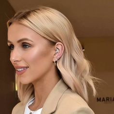 a woman with blonde hair wearing earrings and a beige jacket is smiling at the camera