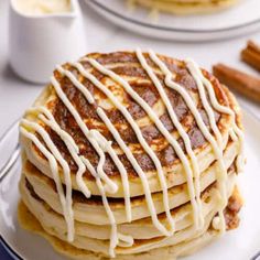 a stack of pancakes covered in icing on a plate with cinnamon sticks next to it