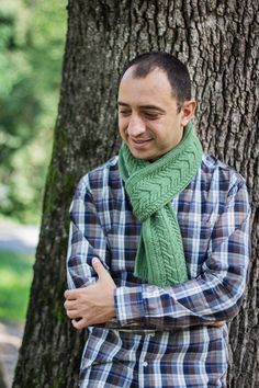 a man standing in front of a tree wearing a green scarf and plaid shirt with his arms crossed