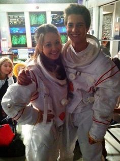 two people in white space suits standing next to each other with their arms around each other