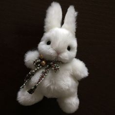 a white stuffed rabbit with a bell around its neck and beaded bells on it's chest