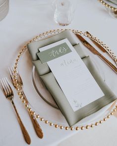 a place setting with silverware and napkins on a white table cloth, along with gold beaded place settings