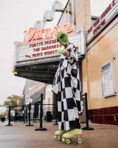 a person dressed as an alien riding a skateboard in front of a movie theater