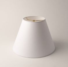 a white lamp shade with a gold ring on the top and bottom, against a gray background