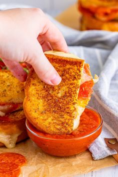 a person is dipping something into a bowl with tomato sauce on the side and another sandwich in the background