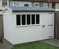 a white shed sitting in the middle of a yard next to a fence and building