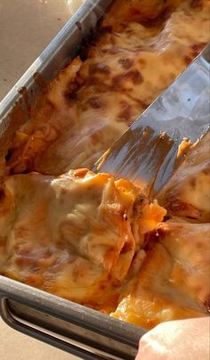 a person holding a spatula in a pan filled with lasagna casserole