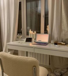 a laptop computer sitting on top of a white desk next to a window with curtains