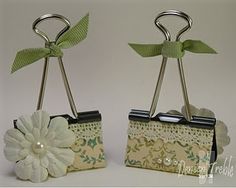 two small boxes with flowers on them are sitting side by side, one has a green bow and the other has a white flower