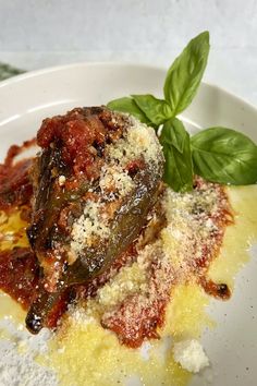 a white plate topped with meat covered in sauce and cheese next to green leaves on top of it