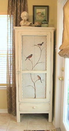 a white cabinet with birds painted on the front and side doors, next to a window