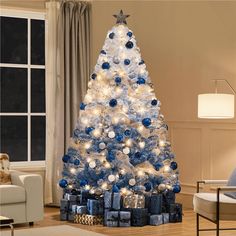 a blue and white christmas tree in a living room with presents on the floor next to it