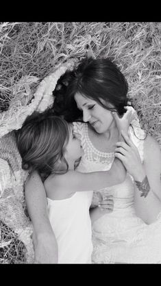 two women are laying on the ground hugging each other in black and white photo with hay behind them