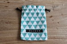 a teal and white patterned pouch with the word oliver on it sitting on top of a wooden table