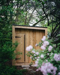 a wooden outhouse surrounded by trees and flowers