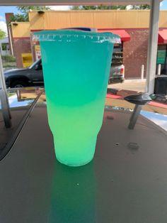 a blue and green cup sitting on top of a table next to a gas station