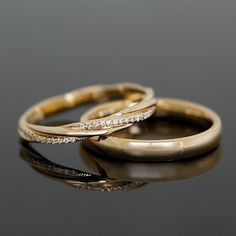 two gold wedding rings with diamond accents on a reflective surface in front of a black background