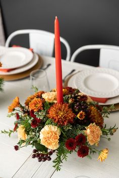 an arrangement of flowers and candles on a dining room table with white plates, napkins and place settings