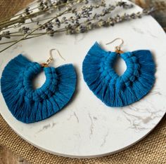 a pair of blue tasseled earrings sitting on top of a white plate next to dried flowers