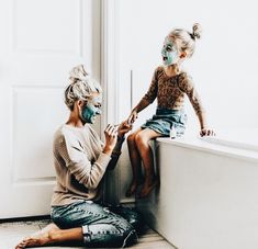 a woman and child with face paint sitting on the edge of a bathtub in front of a door