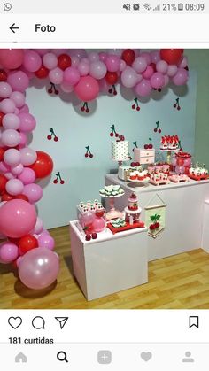 a table filled with lots of pink and red balloons next to a white counter topped with cupcakes