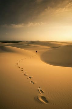 a lone person walking across the desert with footprints in the sand as the sun sets