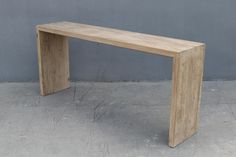 a wooden bench sitting on top of a cement floor next to a gray wall,