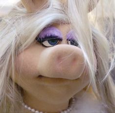 a close up of a stuffed animal with long hair and purple eyeshadow on