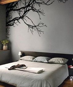 a bed with white sheets and pillows under a tree branch wall decal in a bedroom