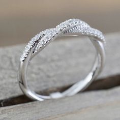 a white gold wedding ring with diamonds on the top and bottom, sitting on a piece of wood