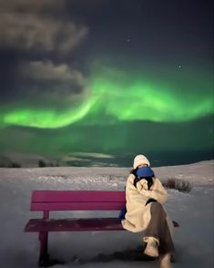 a person sitting on a bench in the snow with an aurora bore behind them and green lights