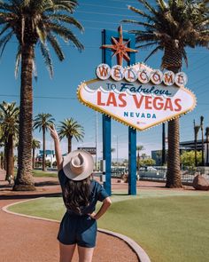 a woman standing in front of the welcome to las vegas sign with her hand up