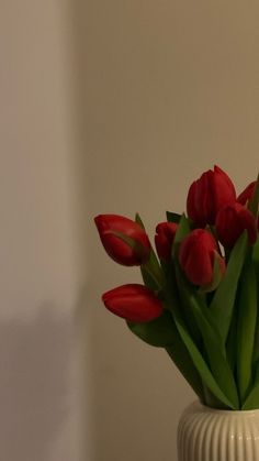 a white vase filled with red tulips on top of a table