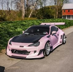 a pink and black car parked on the side of a road in front of some bushes