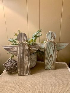 two wooden angel figurines sitting on top of a table next to a plant