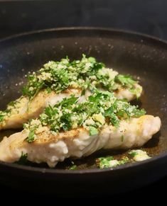 two pieces of fish in a frying pan with parsley on the top and green garnish on the bottom