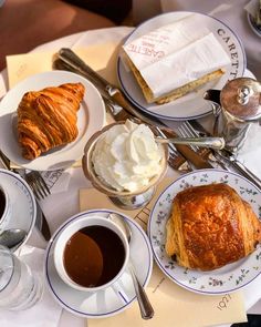 a table topped with plates and cups of coffee next to croissants covered in whipped cream