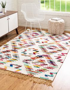 a white chair sitting on top of a wooden floor next to a rug covered in multicolored shapes