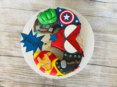 a birthday cake decorated with superheros and stars on a white plate sitting on a wooden table