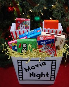 a movie night gift basket with popcorn, movies and snacks in it next to a christmas tree