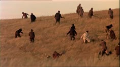 a group of people walking up a hill in the middle of an open field with tall grass